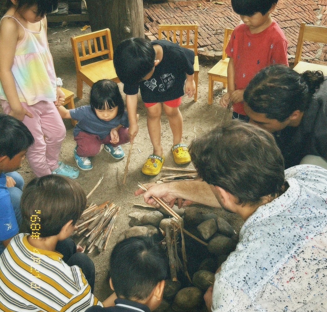 Children observing a ladybug during a nature study session at Firefly Forest School in Bangkok.