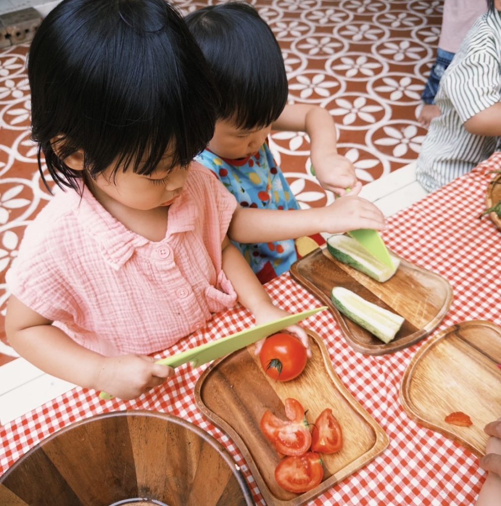 Toddlers composting food scraps during an eco-friendly preschool activity at Firefly Forest School in Bangkok.

