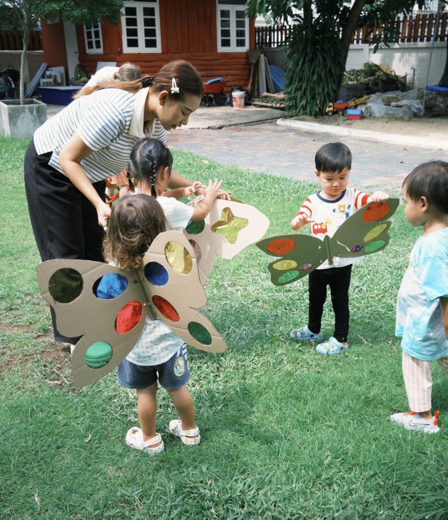 A toddler chasing a butterfly while learning its name in Thai during a bilingual preschool activity at Firefly Forest School.

