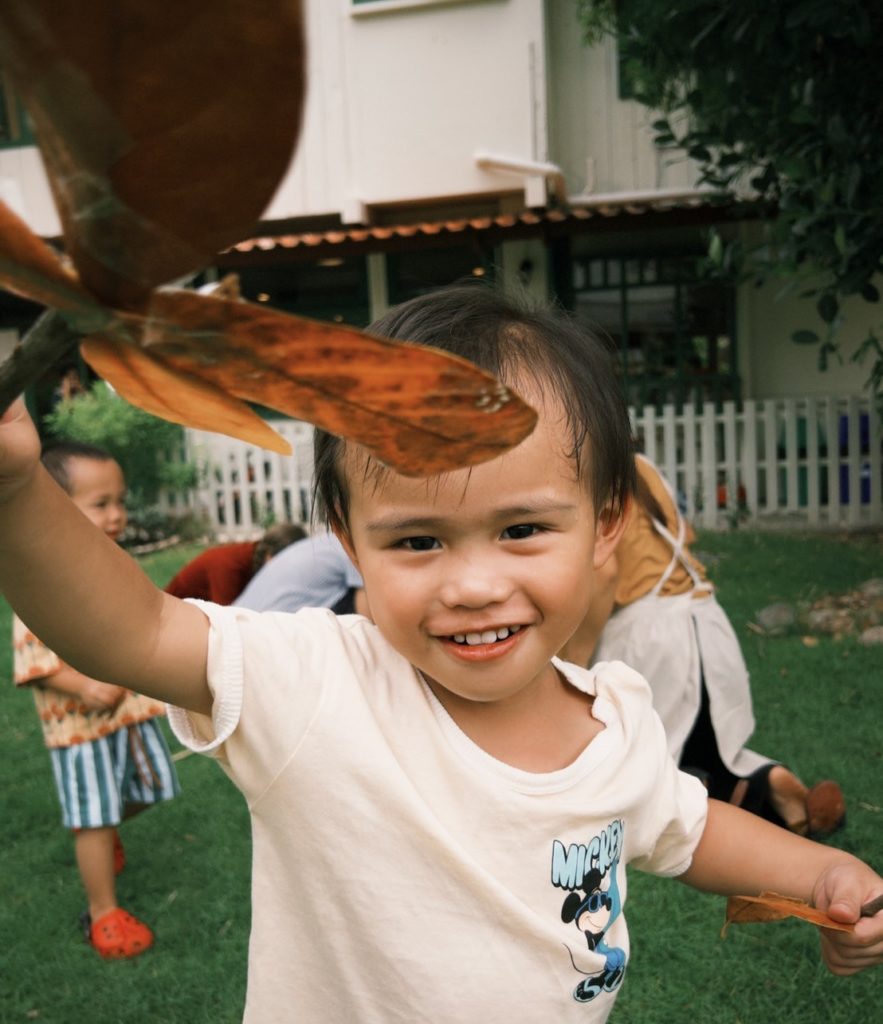 A group of kids creating a nature mural with leaves at Firefly Forest School’s kindergarten in Bangkok.

